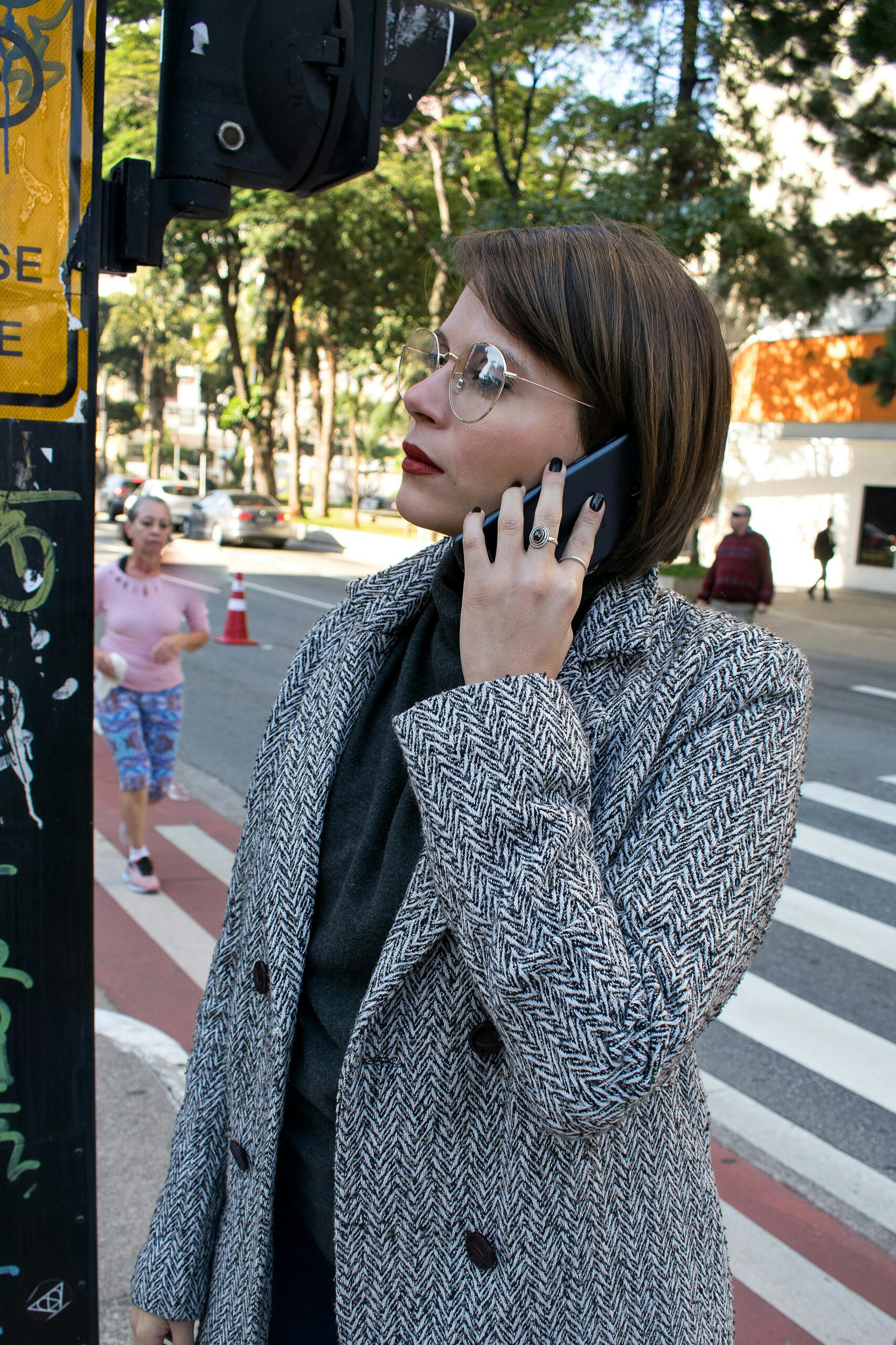 A stylish woman in a coat uses her smartphone at a city crosswalk.